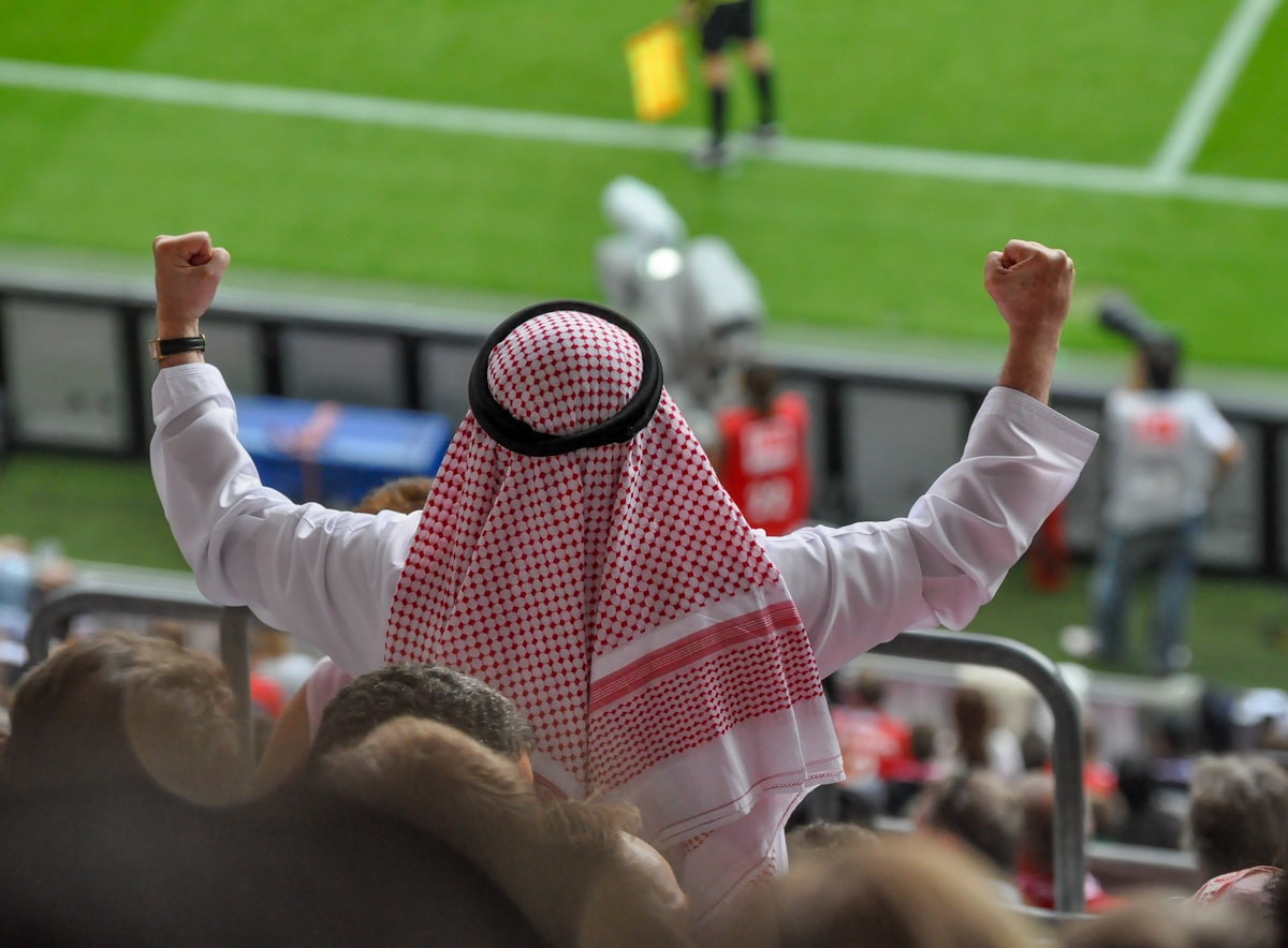Man in traditional Arab clothing cheering at a soccer game